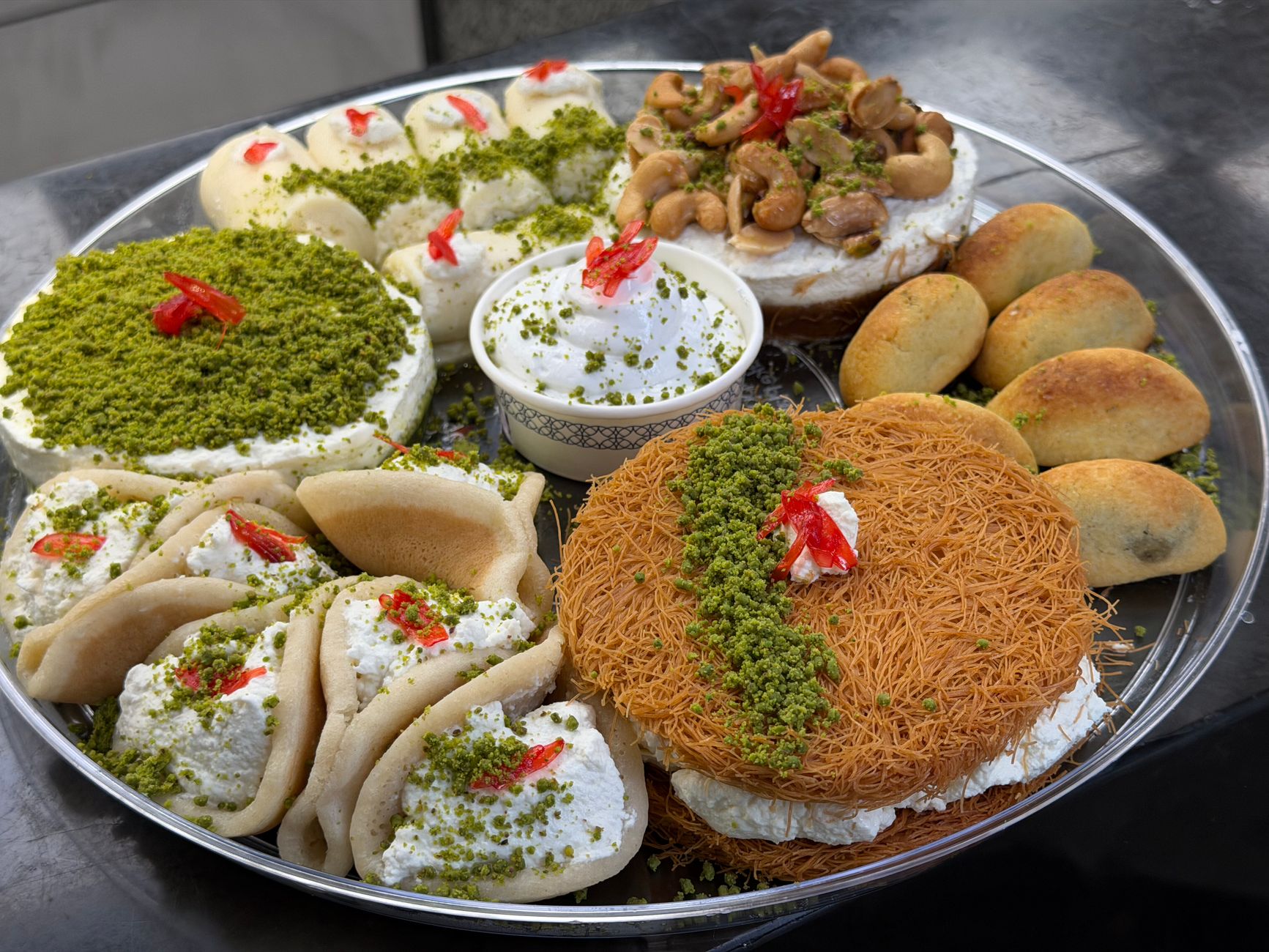A vibrant platter of Middle Eastern desserts featuring kunafa, qatayef, and pastries topped with nuts and cream.