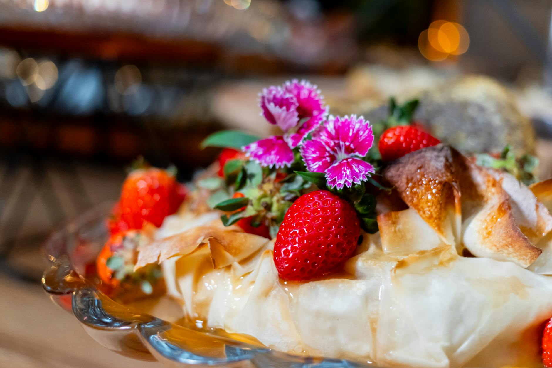 Close-up of a pastry topped with fresh strawberries and purple flowers — la "flor" de pasta filo