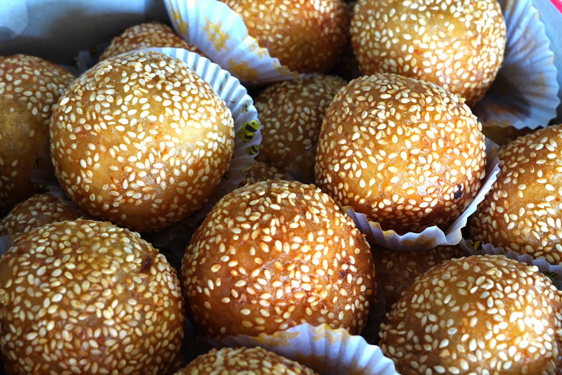 Close-up of golden sesame balls, freshly baked and presented in paper cups, showcasing their appetizing texture. — briwat y p