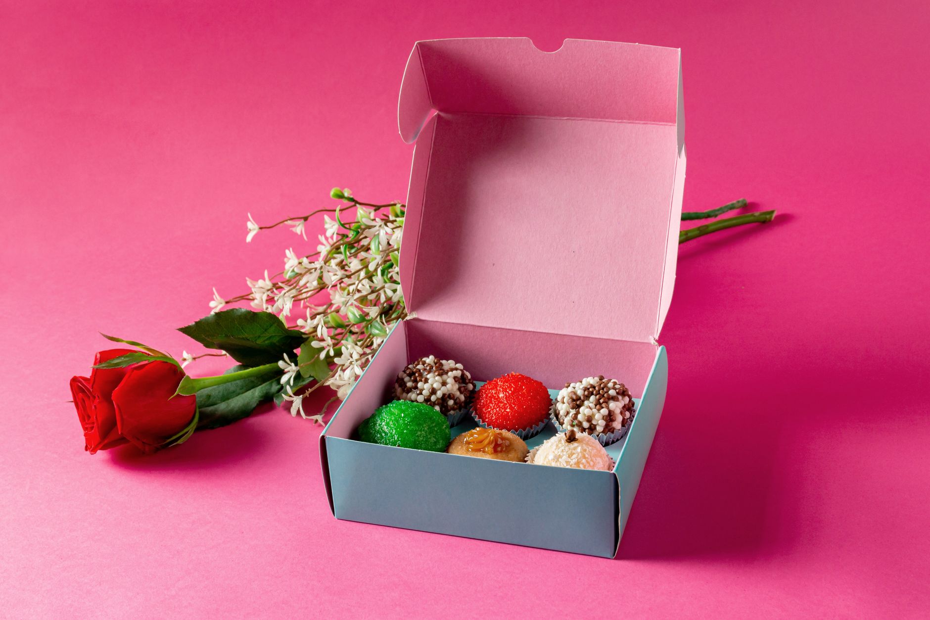 Colorful cupcakes presented in an open box with roses on a vibrant pink background.